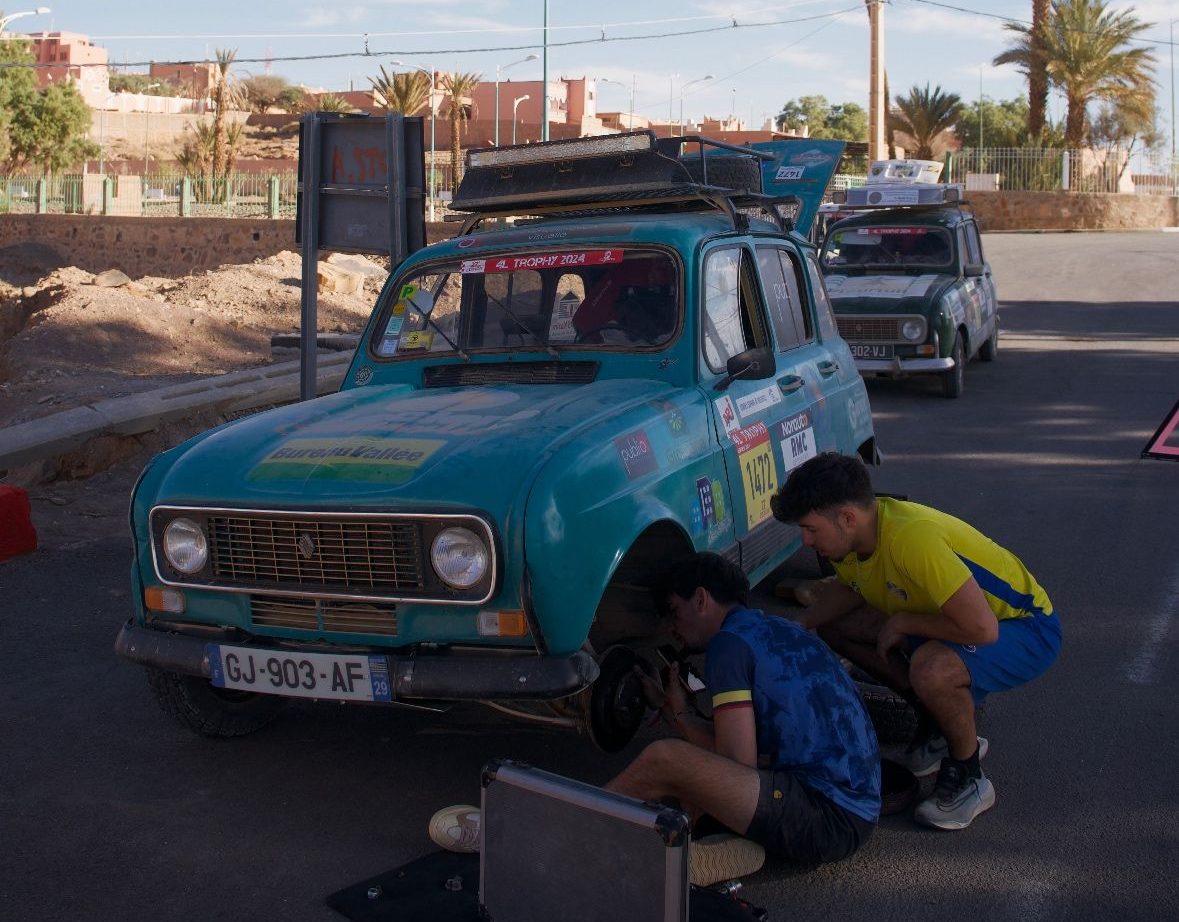 Deux membres de l’équipage du 4L Trophy de l’ECAM Louis de Broglie effectuent une réparation sur leur Renault 4L bleue garée au bord de la route.
