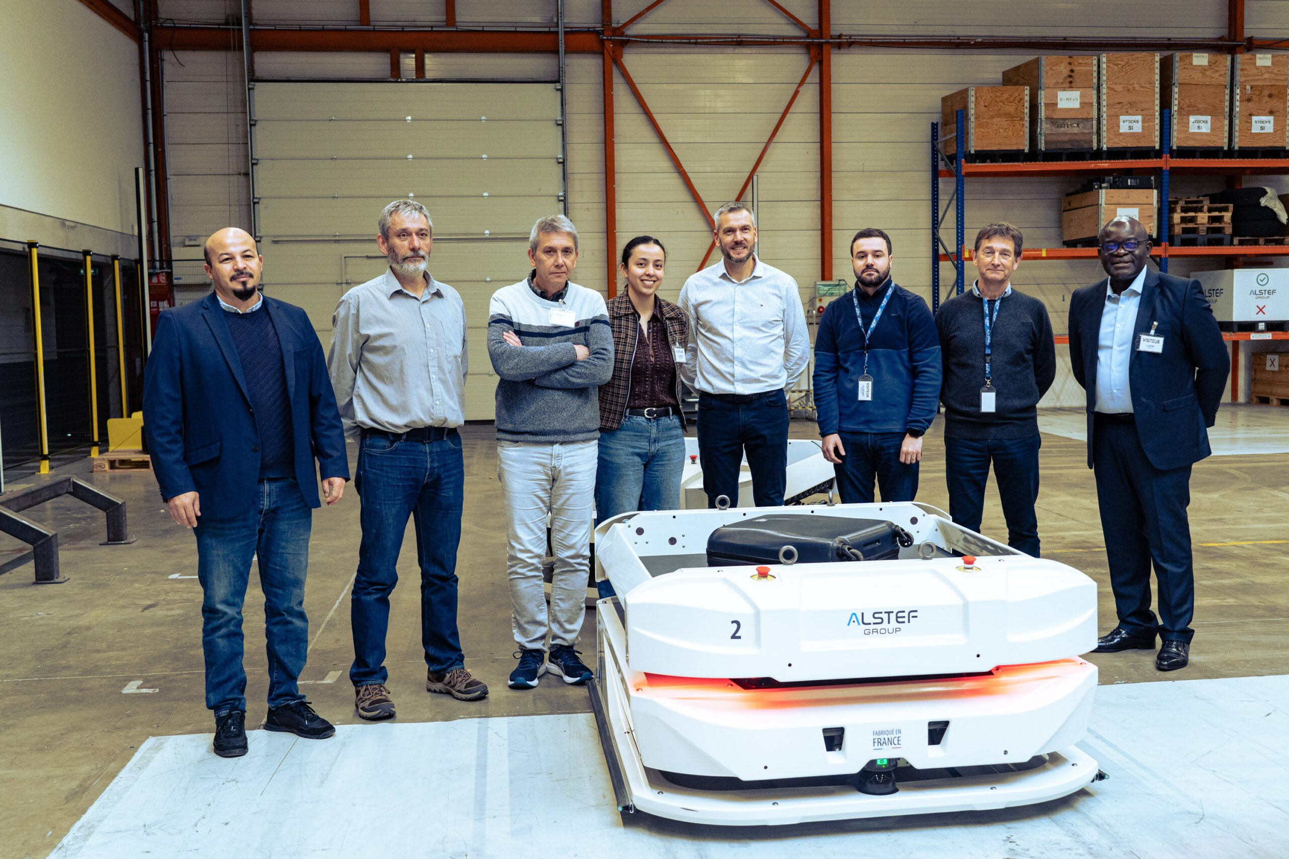Photo de groupe réunissant les partenaires du projet ALPHA (Alstef Group, Secure-IC, IMT Atlantique et ECAM Louis de Broglie) devant un véhicule autonome AGV.